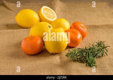 Eine Nahaufnahme von Zitronen, Mandarinen und Rosmarin auf einem Stoff Stockfoto