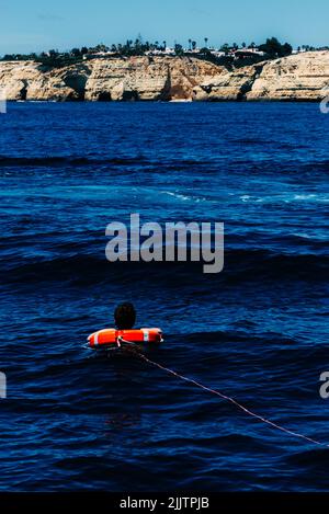 Eine vertikale Aufnahme einer Person mit einer roten Rettungsboje an einer Bucht der Algarve, Portugal Stockfoto