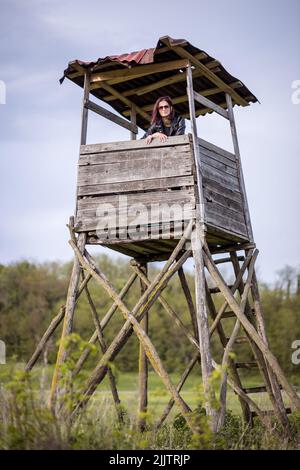 Eine schöne Aufnahme einer jungen kaukasischen Frau, die an einem sonnigen Tag auf einem alten hölzernen Wachturm im Park gegen den bewölkten Himmel steht Stockfoto