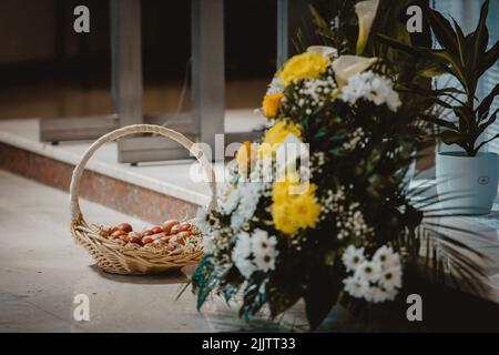 Ein Strohkorb mit schön dekorierten roten Ostereiern neben einem Strauß Stockfoto