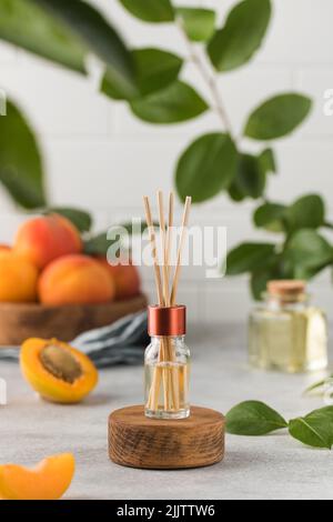 Innenparfüm mit dem Duft von Aprikosen. Glas mit Aromaöl und Banbu-Sticks Stockfoto