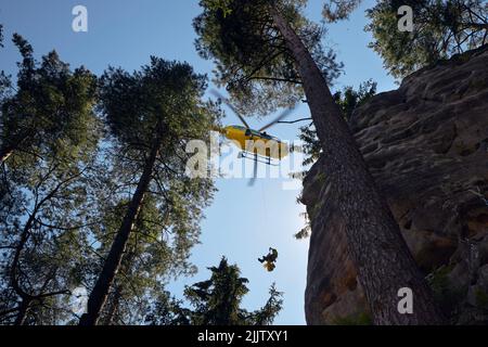 Adrspach, Tschechische Republik - 24. Juli 2022: Der Rettungsarzt, der per Seil unter dem Hubschrauber aufgehängt wird, steigt in schwer zugänglichen felsigen Untergrund ab Stockfoto