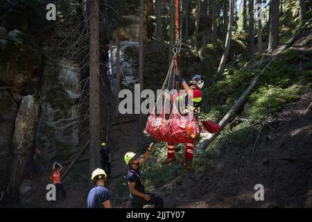 Adrspach, Tschechische Republik - 24. Juli 2022: Notarzt, der während der Rettung des verletzten Touristen aus dem Diff am Seil unter dem Hubschrauber aufgehängt wurde Stockfoto