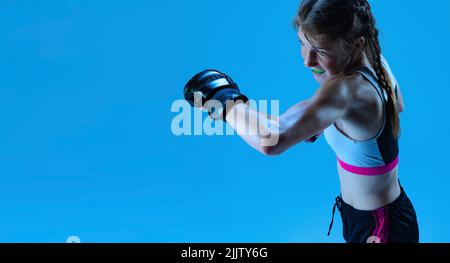 Juniorliga. Junges Mädchen MMA Kämpfer üben Punsch isoliert auf blauem Hintergrund in Neonlicht. Konzept von Sport, Wettbewerb, Aktion, Leistungen Stockfoto