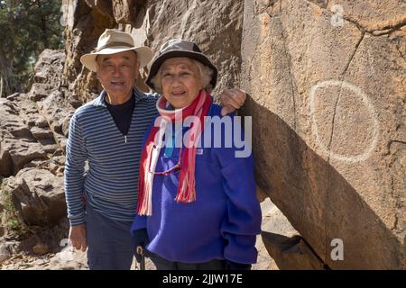 Maurice Lee (86) und seine Frau Wilma Lee (83), gebürtiger Australier, aus China, tourten durch den Sacred Canyon in den Flinders Ranges in Südaustralien. Sowohl Maurice als auch Wilma aktive Senioren gaben erst vor ein paar Jahren das Skifahren auf. Jetzt reisen sie, um ihre Liste der Orte zu füllen, die sie schon immer in Australien besuchen wollten. Sie sind dabei, ihren Hochzeitstag 62. zu feiern. Das Foto zeigt Maurice und Wilma, mit einer der Aborigines-Perraglyphen im Sacred Canyon, die in der Nähe von Wilpena Pound liegt. Stockfoto
