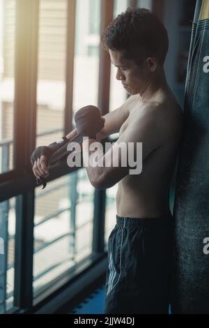 Eine junge Passform bestimmte südostasiatische männliche Boxer, der sein Handgelenk für das Training einwickelte Stockfoto