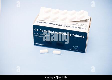 Schachtel mit 100 Cocodamol 30 500 mg Tabletten mit Blisterpackung und loser Tablette auf Karton, isoliert auf pastellblauem Hintergrund. Konzept der Opioidkrise Stockfoto