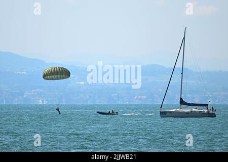 Langenargen Am Bodensee, Deutschland. 28.. Juli 2022. Fallschirmjäger landen mit ihren Fallschirmen vor Langenargen am Bodensee, um Wasserlandungen zu üben, während ein Segelboot über den Bodensee segelt. Kurz darauf werden die Fallschirmjäger von Kameraden in Schlauchbooten aus dem Wasser geholt. Quelle: Felix Kästle/dpa/Alamy Live News Stockfoto