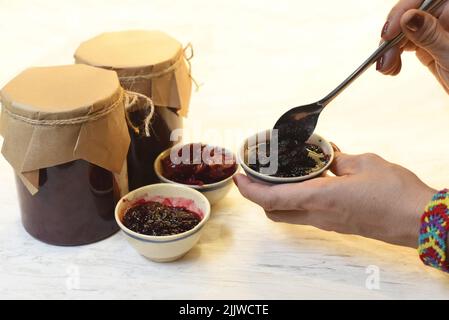 Eine Hand, die hausgemachte Maulbeermarmelade in kleinen Schüsseln aus Gläsern serviert Stockfoto