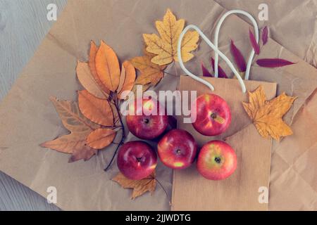 Verpackung in Kraftpapier mit herbstlichen gelben Blättern und Äpfeln. Herbsthintergrund. Flach liegend. Speicherplatz kopieren. Stockfoto