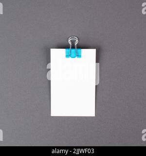 Leeres weißes Papier mit Büroklammer auf grauem Hintergrund, Platz für Text, Erinnerung oder Nachricht im Büro, Kommunikationskonzept Stockfoto