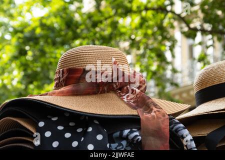 Weibliche Korbhüte mit verschiedenen Bögen zum Verkauf und grüne Straße im Hintergrund. Paris, Frankreich. Stilvolle Mode, Sommerurlaub, Strandurlaub entspannen Stockfoto