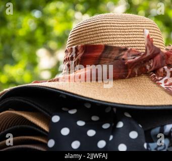 Weibliche Korbhüte mit verschiedenen Bögen zum Verkauf und grüne Straße im Hintergrund. Paris, Frankreich. Stilvolle Mode, Sommerurlaub, Strandurlaub entspannen Stockfoto