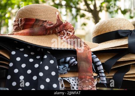 Weibliche Korbhüte mit verschiedenen Bögen zum Verkauf und grüne Straße im Hintergrund. Paris, Frankreich. Stilvolle Mode, Sommerurlaub, Strandurlaub entspannen Stockfoto