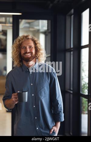 Porträt eines lächelnden kaukasischen jungen Geschäftsmannes mit Kaffeebecher, der im kreativen Büro steht Stockfoto