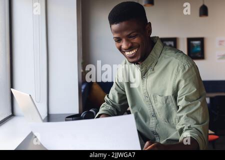 Lächelnder afroamerikanischer junger Geschäftsmann, der das Dokument im Büro untersucht Stockfoto