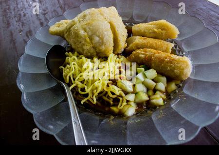 Empek-Empek ist gebratener Fisch und Tapioka, Gurkenscheiben, gelbe Nudeln mit süß-saurer Sauce namens Essigsauce oder Essigsauce serviert. Serviert Stockfoto