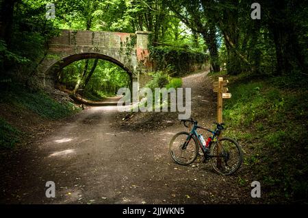 Ein Holdsworth-Schotterfahrrad ist an einem Wegweiser auf dem Downs Link, einer stillgesteerten Eisenbahnlinie in West Sussex, Großbritannien, angelehnt. Stockfoto