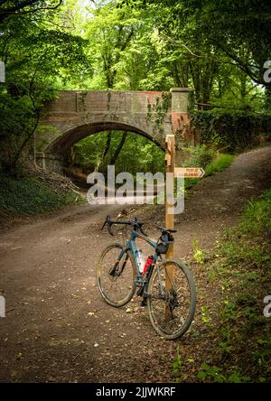 Ein Holdsworth-Schotterfahrrad ist an einem Wegweiser auf dem Downs Link, einer stillgesteerten Eisenbahnlinie in West Sussex, Großbritannien, angelehnt. Stockfoto
