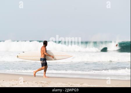 Ein Surfer, der Surfbrett hält und am Strand in Puerto Escondido, Mexiko, läuft Stockfoto