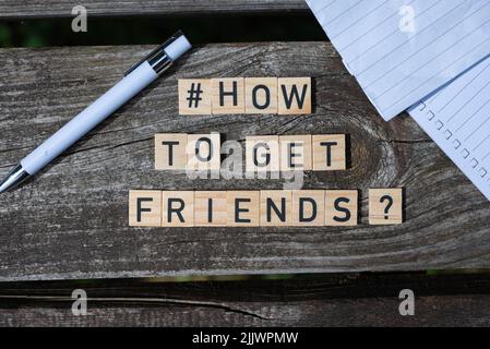 Wie man Freunde bekommt Frage Buchstaben auf Holzblöcken auf einem Holztisch mit Bleistift und Papier an den Seiten des Schusses Stockfoto