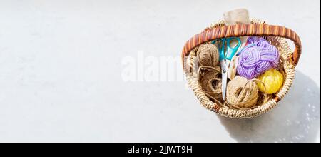 Auf der hellen Oberfläche des Tisches befindet sich der Korbkorb, in dem die Kugeln der mehrfarbigen Wollfäden sind. Negatives Leerzeichen links. Stockfoto