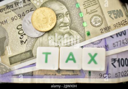 Ein selektives Fokusbild von indischen Währungshinweisen und Münzen mit Steuerbriefen darüber. Das Finanzierungskonzept umfasst GST, Einkommenssteuer Stockfoto