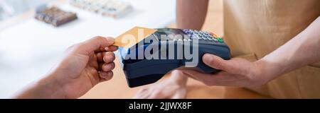 Beschnittene Ansicht des Verkäufers, der Terminal in der Nähe eines afroamerikanischen Kunden mit Kreditkarte in Süßwaren hält, Banner Stockfoto
