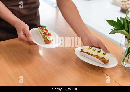 Beschnittene Ansicht des afroamerikanischen Verkäufers, der Dessert in einem Süßigkeitenladen hält Stockfoto