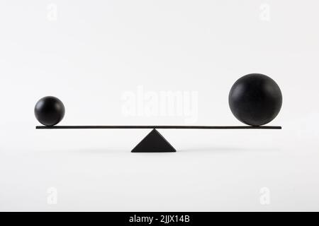 Kleine und große schwarze Kugeln balancieren auf minimalistischen Stil geometrische Skalen vor weißem Hintergrund Stockfoto