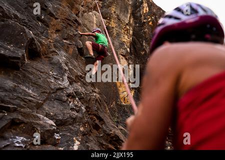 Blick in den niedrigen Winkel auf aktive ältere männliche und weibliche Bergsteiger, die auf felsigen Klippen klettern Stockfoto