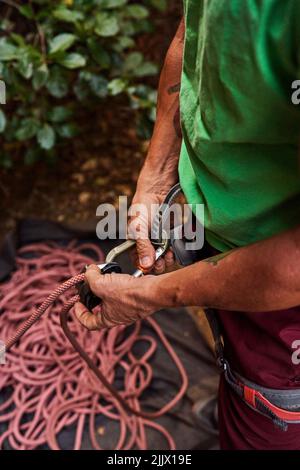 Hochwinkelansicht eines aktiven männlichen Kletterers, der Kletterseil mit Karabiner am Geschirr befestigt Stockfoto