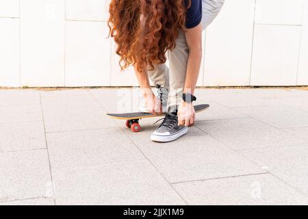 Die ganze Länge der jungen Frau, die Schnürsenkel bindet, während sie auf dem Skateboard steht Stockfoto