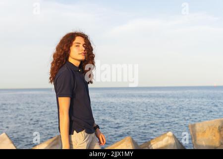 Porträt einer jungen Frau mit roten Haaren, die am Strand gegen den Himmel steht Stockfoto