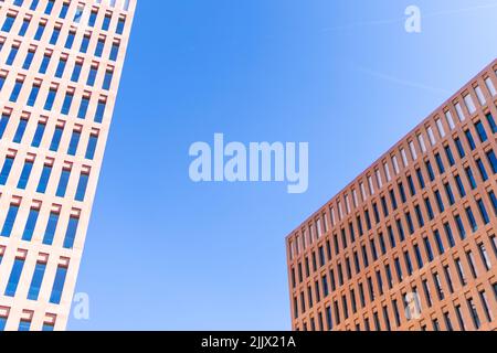 Von unten graue Fassade des modernen mehrstöckigen Hauses mit vielen Fenstern, die sich am sonnigen Sommertag in der Stadt gegen den wolkenlosen blauen Himmel befinden Stockfoto