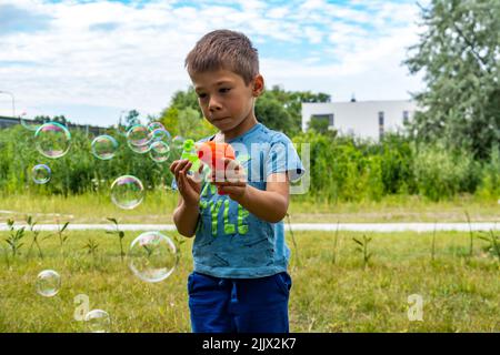 Ein süßer junger polnischer kaukasischer Junge, der an einem sonnigen Tag Seifenblasen im Freien erzeugt Stockfoto