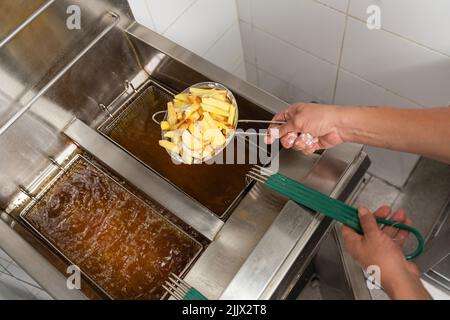 Von oben vom Ernte anonymen Koch, der Pommes frites in frittierten Korb in kochendem Öl macht, während er in der hellen Küche arbeitet Stockfoto