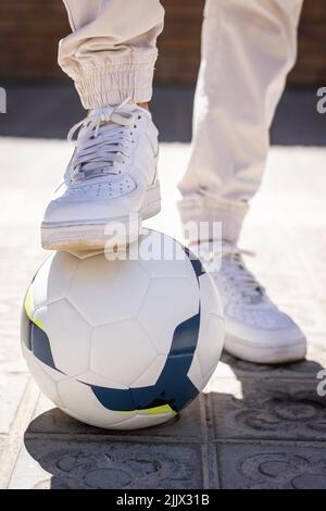 Beschnitten, unerkennbar, wenn ein junger Mann mit einem Fuß über dem Fußball auf dem Fußweg steht Stockfoto