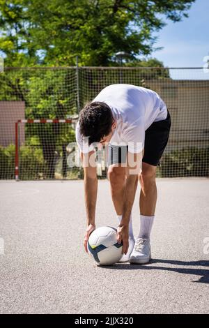 Ganzer Körper eines jungen Mannes, der beim Fußballspielen den Ball auf dem Fußballplatz platziert Stockfoto