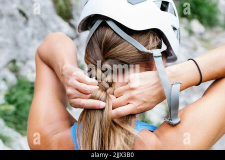 Rückansicht einer Frau mit Sicherheitshelm, der während der Vorbereitung auf das Wandern ein Geflecht bindet Stockfoto