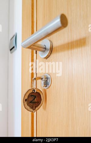 Niedriger Schlüsselwinkel mit rundem Ziffernschild, der bei Tageslicht an der Holztür im Hotelzimmer hängt Stockfoto