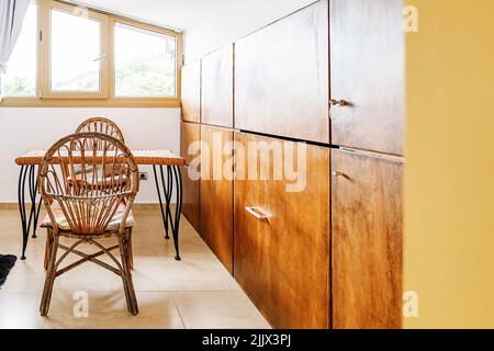 Kleiner Tisch mit Stühlen und Vintage-Holzschrank im gemütlichen Mansardenzimmer des Hauses am sonnigen Tag auf dem Land Stockfoto