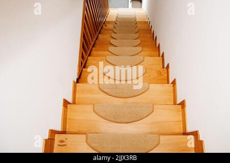 Von oben führt eine Holztreppe zum Flur eines modernen Hauses mit weißen Wänden am Tag Stockfoto