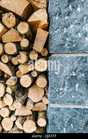 Stapel von gehacktem Brennholz, gestapelt in der Nähe einer Steinmauer im Haus tagsüber auf dem Land Stockfoto
