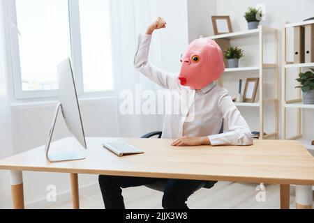 Verrückte lustige Geschäftsfrau Arbeiter Freiberufler in rosa Fischmaske Arbeit am Computer online zeigt Muskeln in hellen modernen Büro. Speicherplatz kopieren Stockfoto