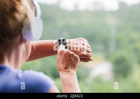 Hände einer älteren Frau, die vor dem Training die Fitness-Smartwatch und Kopfhörer aufsetzt Stockfoto