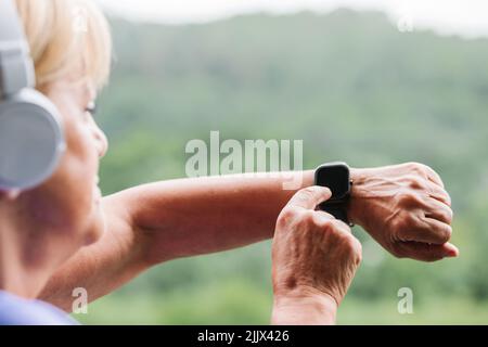 Hände einer älteren Frau, die vor dem Training die Fitness-Smartwatch und Kopfhörer aufsetzt Stockfoto