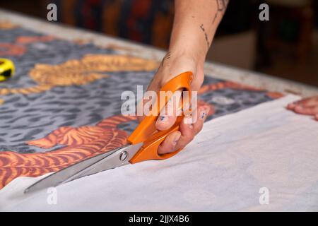 Anonyme Erwachsene Designerin schneidet Stoff mit einer Schere, die im Studio auf der Werkbank steht Stockfoto