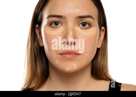 Junge Frauen posieren mit Concealer unter ihren Augen und Gesicht auf weißem Hintergrund Stockfoto