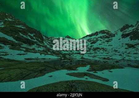 Landschaft von felsigen Klippen mit schneebedeckten Gipfeln am Ufer der Nordsee unter hellen aurora Borealis Lichtern im Agvatnet See Stockfoto